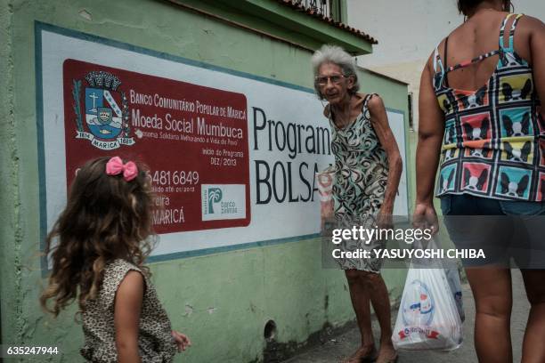 Women walk in front of a wall advertising the "Mumbuca" card in Marica, surburb of Rio de Janeiro, Brazil, on February 8, 2017. Mumbuca, the first...