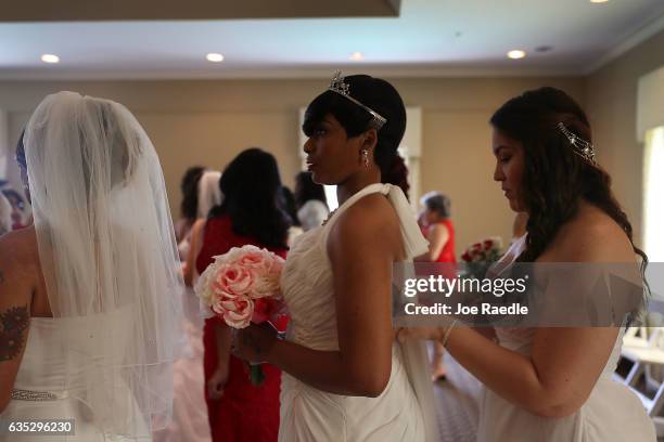 Tierra Hunter gets help with her wedding dress from, Madelina de la Cruz as they prepare to participate in a group Valentine's day wedding ceremony...