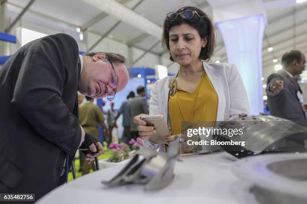 An attendee takes a photograph with a smartphone of Hindustan Aeronautics Ltd. 3D printing aircraft engine components on display at the company's...
