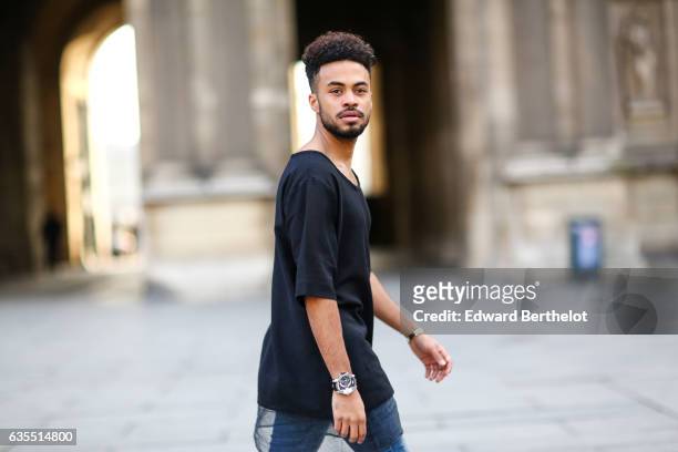 Theo Kimbaloula, fashion blogger, wears a Zwitter Paris black t-shirt, Asos blue denim jeans, and Asos boots, on February 12, 2017 in Paris, France.