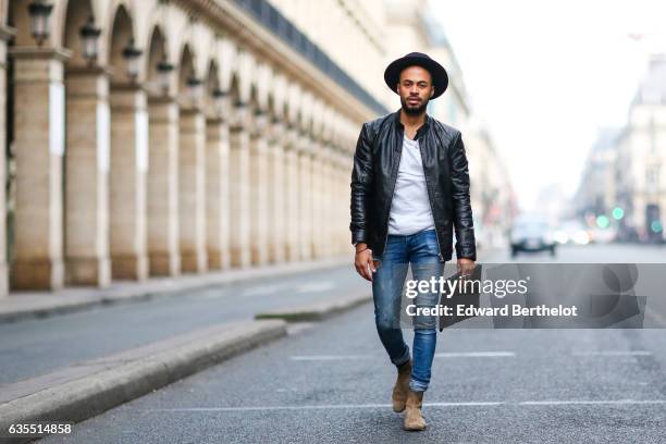 Theo Kimbaloula, fashion blogger, wears a Sand Copenhagen black leather jacket, a Baan Bag black clutch, Asos blue denim jeans, and The Kooples brown...