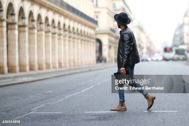 Theo Kimbaloula, fashion blogger, wears a Sand Copenhagen black leather jacket, a Baan Bag black clutch, Asos blue denim jeans, and The Kooples brown...