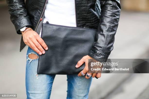 Theo Kimbaloula, fashion blogger, wears a Sand Copenhagen black leather jacket, a Baan Bag black clutch, Asos blue denim jeans, and The Kooples brown...