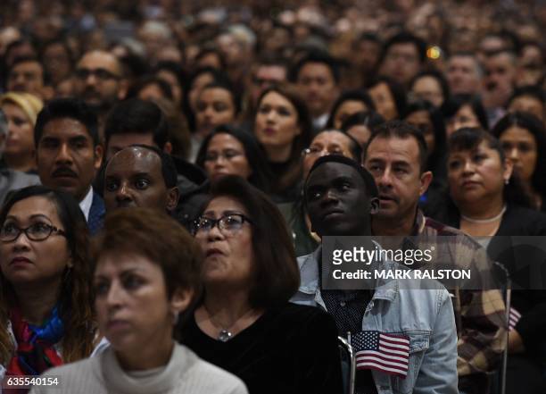 People listen to a speech before pledging allegiance to the United States of America as they receive US citizenship at a naturalization ceremony for...