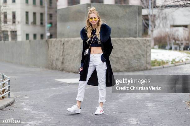 Chiara Ferragni wearing white pants, cropped top, sneaker, black coat with fur collar outside Michael Kors on February 15, 2017 in New York City.