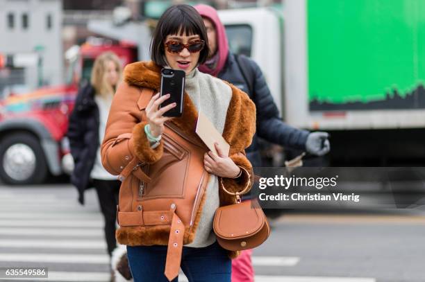 Eva Chen filming with her phone wearing a Chloe bag, brown sheepskin leather jacket outside Michael Kors on February 15, 2017 in New York City.