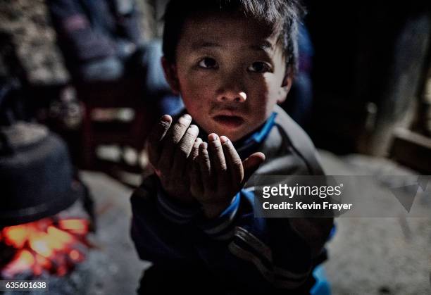 Left behind' child Luo Lie keeps warm by a fire in the family home on December 17, 2016 in Anshun, China. Like millions of Chinese children, the four...