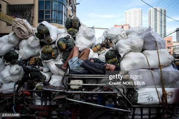 Worker sleeps on a rickshaw full of pumpkins along a street in Divisoria Market in Manila on February 16, 2017. / AFP / Noel CELIS