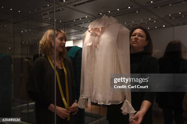 Staff members adjust a 1981 Emanuel pale pink chiffon blouse with satin neck-ribbon worn during Diana's first official portrait in 1981 during a...