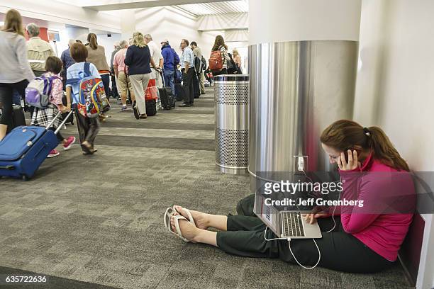 Woman sat on the floor in Los Angeles, LAX, international airport charging her laptop.