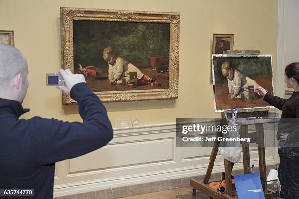 Man taking a picture of a woman copying a painting called 'Baby at Play' in the National Gallery of Art.