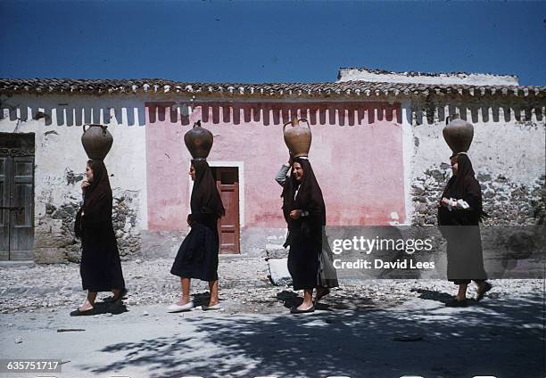 Four girls from the village of Ploaghe carry water jars balanced on their head. | Location: Ploaghe, Sardinia.