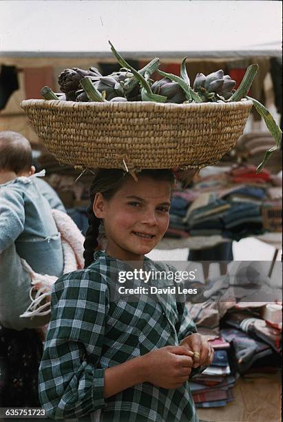 Girl balances a basket of artichokes on her head on market day in the village of Ploaghe, Sardinia. | Location: Ploaghe, Sardinia, Italy.
