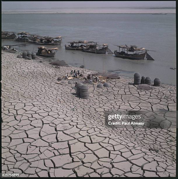 With boats tied up offshore, men prepare to weave baskets while their familes sit nearby, on the shores of the Indus River. Pakistan.