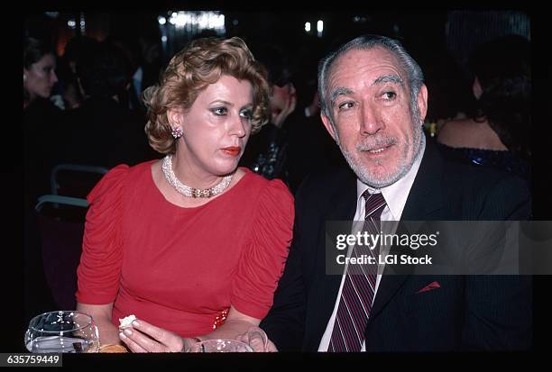 Picture shows actor, Anthony Quinn, and his current wife, Yolanda, seated at a table together. He is dressed in a suit and she is in a pink dress...