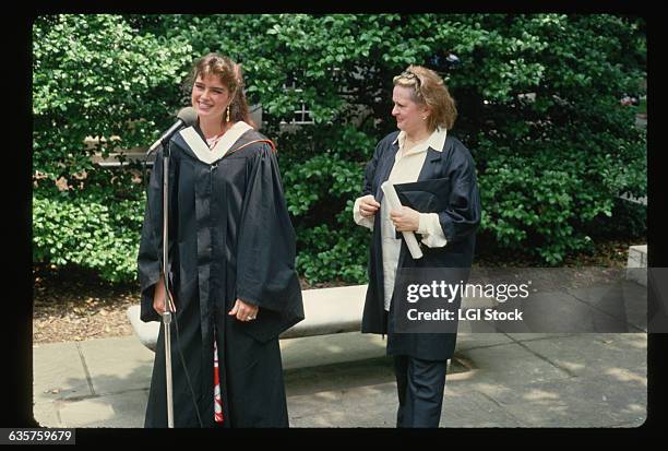 Actress Brooke Shields wears a graduation gown as she speaks into a microphone on her graduation day at Princeton University.