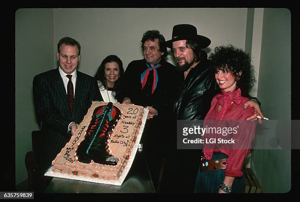 Man presents country legends Johnny Cash and Waylon Jennings a cake with a cowboy boot backstage at on of their concerts together at Radio City Music...