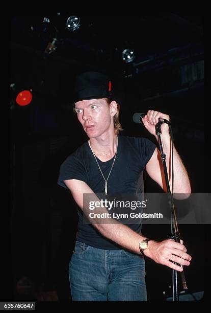Picture shows writer/poet/singer, Jim Carroll, performing in concert. He is holding on to a microphone with both hands and standing to the side of...