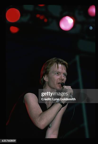 Singer/songwriter/novelist Jim Carroll is shown singing on stage in concert, wearing a black shirt with the sleeves cut off.
