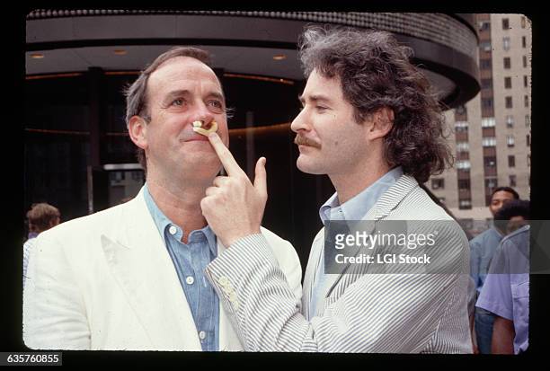 Kevin Kline pushes a french fry up John Cleese's nose in front of a theater.