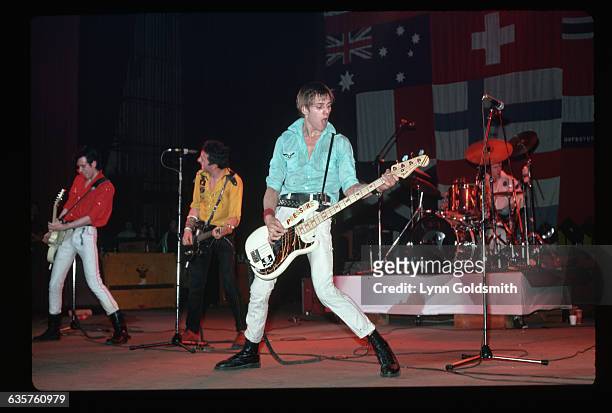 The picture shows the band The Clash performing on stage. In the background of the picture is a multi-cultural flag hanging.