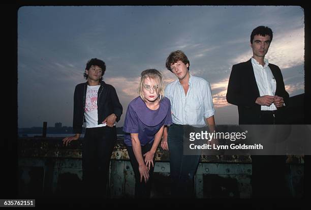 Photo shows the rock and roll group The Talking Heads posed on what appears to be a pier. Left to right: Jerry Harrison, Tina Weymouth, Chris Frantz...
