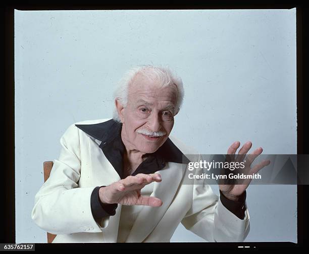 Picture shows conductor of the Boston Pops Orchestra, Arthur Fiedler, seated in a studio with his hands placed out in front of him. He is dressed in...