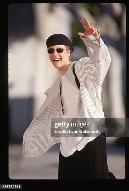 Los Angeles,CA-Jonathan Bbrandis: is shown waving in a street. He is wearing a barite, sunglasses and suspenders with a open buttondown.
