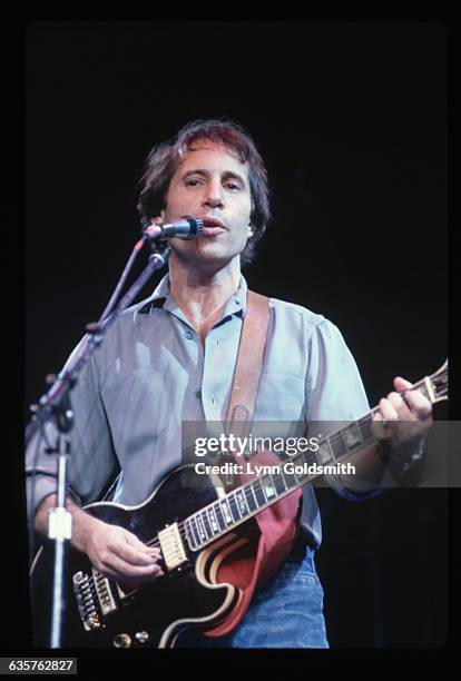 Paul Simon performing. He is shown waist-up, singing and playing guitar. Undated photograph.