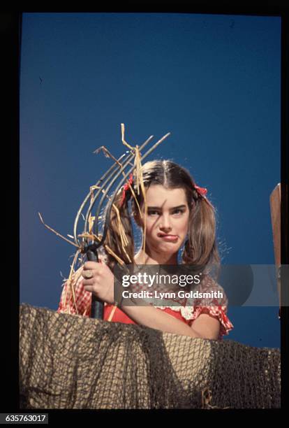 Brooke Shields, dressed as a farmer, holds a pitchfork.