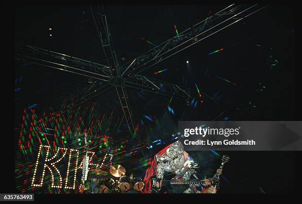 Musician Gene Simmons of the glam-rock band "Kiss" sticks out his infamously long tongue during a performance on stage. He is crouched over his bass...