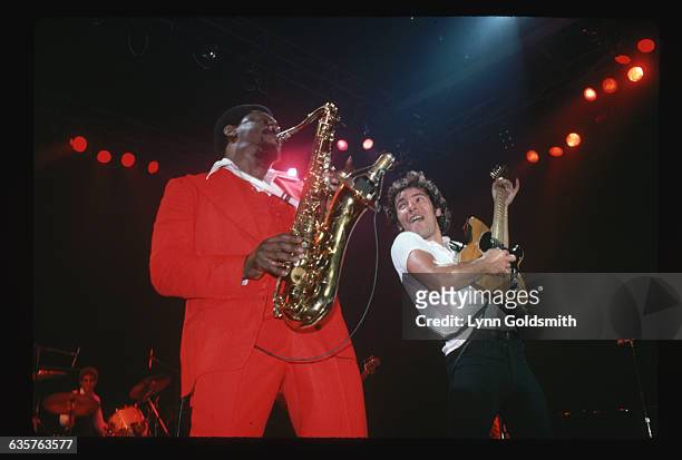 Photo shows rock and roll musician Bruce Springsteen and saxonphonist Clarence Clemmons playing in concert on stage. In the background can be seen...