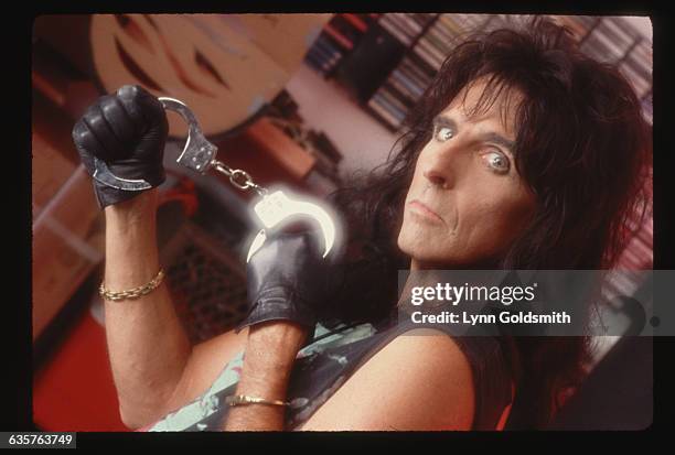 Picture shows Alice Cooper posing inside with a pair of handcuffs. He is shown from the shoulders up and is looking into the camera. He is wearing a...