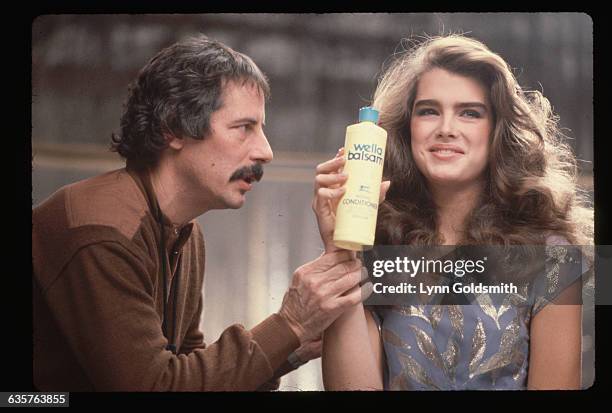 Director stands near actress Brooke Shields who holds a bottle of Wella Balsam shampoo during the filming of a television commercial.