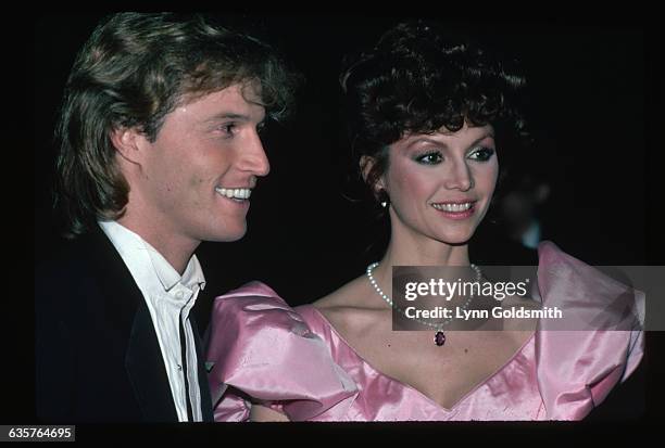 Picture shows actress, Victoria Principal, and singer, Andy Gibb, posing together. She is shown in a pink, satin dress and a pearl necklace. He is in...