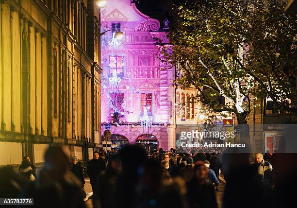 christmas in france crowd passing by the purple-illuminated and painted facade of the iconic christian patisserie - strasbourg winter stock pictures, royalty-free photos & images