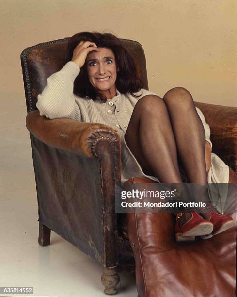 Italian comedian Anna Marchesini posing sitting on an old leather armchair for a studio photo shooting. Italy, 1998