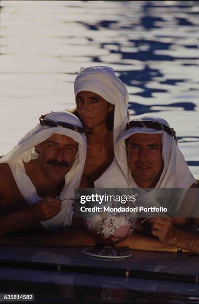 The comic trio formed by Massimo Lopez, Anna Marchesini and Tullio Solenghi posing by a swimming pool in front of a huge ice-cream cup. On their...