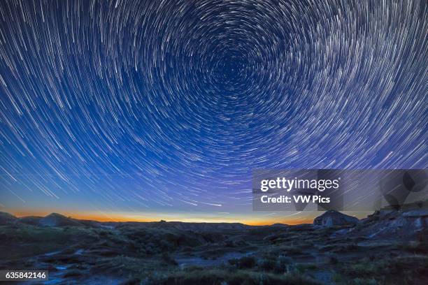 Summer solstice twilight and circumpolar star trails over the badlands of Dinosaur Provincial Park, Alberta. Some bright noctilucent clouds are...