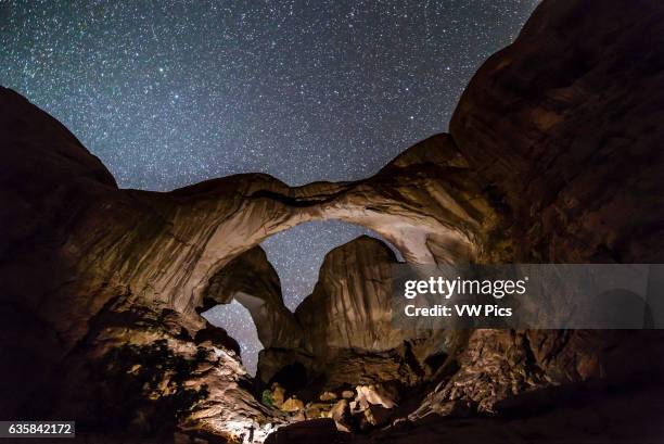 Photographer using a bright light to illuminate Double Arch in Arches National Park, Utah, on a dark night before moonrise provided natural...