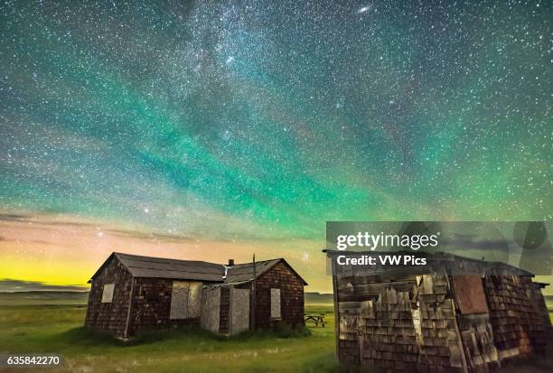 The Pleiades rising behind the rustic cabins and outbuildings of the historic Larson Ranch in Grasslands National Park, Saskatchewan. Aurora shines...