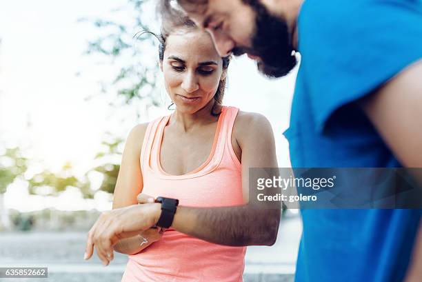latina sportswoman and bearded sportsman looking together on smartwatch - checking sports stock pictures, royalty-free photos & images