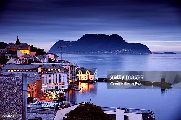 illuminated buildings around the inner harbour of alesund city in norway at dusk. - romsdal stock pictures, royalty-free photos & images