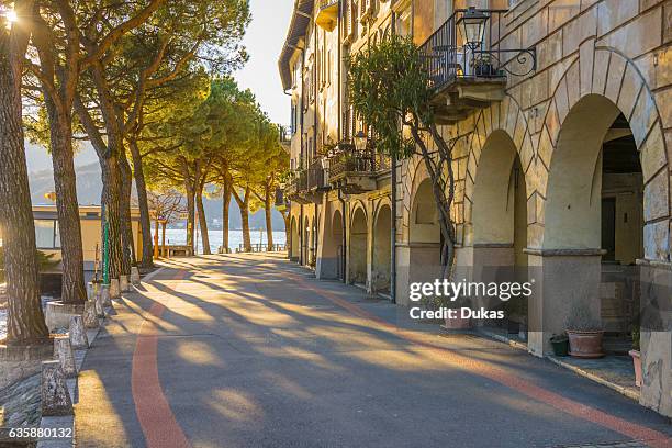 Street with sunlight and old buildings on the waterfront with trees in Morcote, Ticino - Switzerland.
