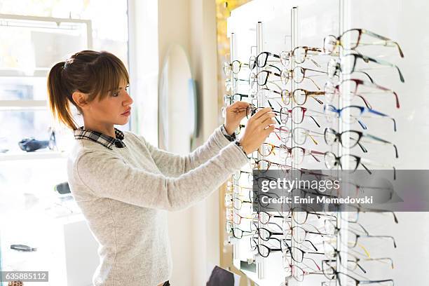 young woman choosing glasses in optical shop - lens optical instrument 個照片及圖片檔