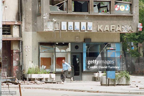 Bosnian man runs in a Sarajevo street where many civilians have been hit by sniper fire. The building behind him has been severely damaged in the war.