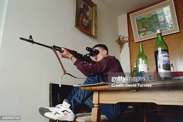 Bosnian sniper attempts to shoot Serbian snipers in the mountains from his position on the 20th floor of a Sarajevo building.