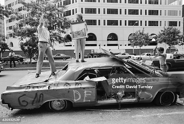 Demonstrators stand atop a destroyed General Motors car during a protest against a deal to raze Detroit's Poletown neighborhood to make room for a GM...