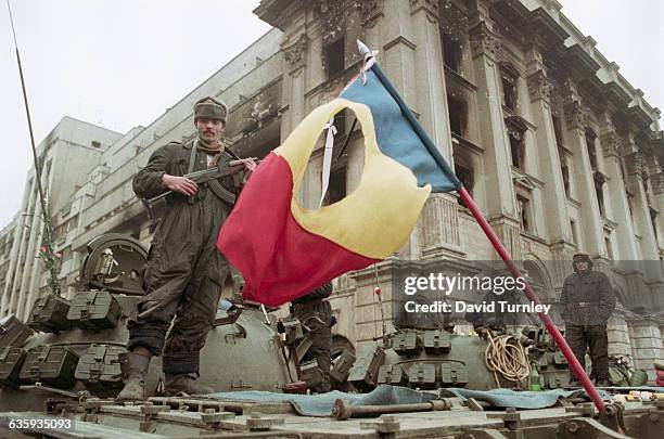 Soldier stands atop a tank with a rifle in Bucharest's Revolution Square after the overthrow of Romanian president Nicolae Ceausescu. In front of him...
