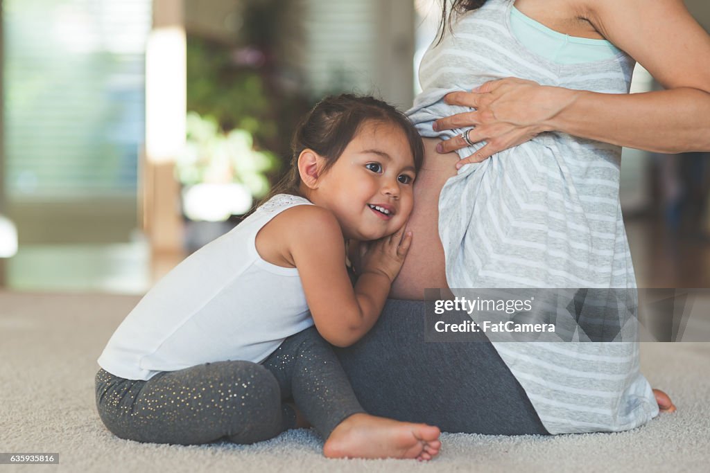 Niña étnica escuchando a su madre embarazada barriga